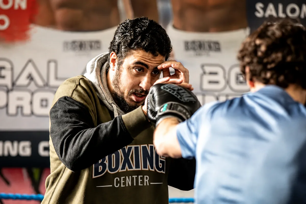 Un coach de Boxing Center Minimes corrige la garde d’un boxeur, gants au visage