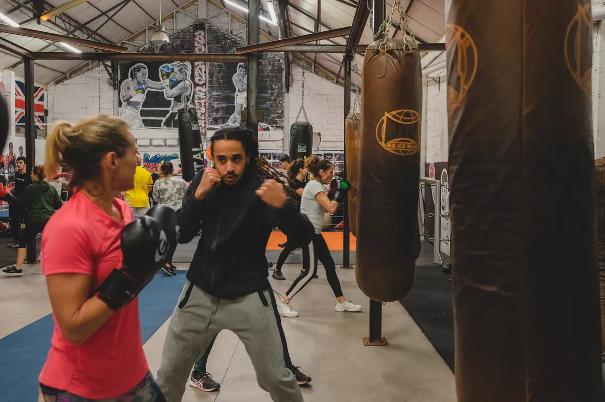 Une coach accompagne un pratiquant débutant en garde pendant un cours collectif